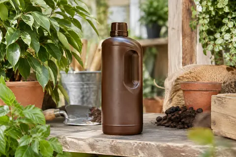 Bidon marron d’engrais liquide pour plantes vertes et ficus posé sur une étagère en bois près de feuillage
