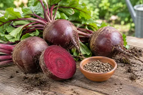 Betteraves rondes rouges avec feuillage frais et quelques graines sur une planche en bois