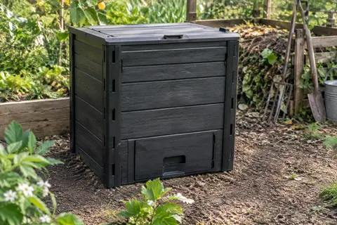 Composteur de jardin noir à l’aspect bois, installé sur la terre dans un espace de jardinage